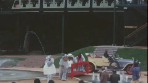 Lord Montagu of Beaulieu The wombles stood in front of a crowd of people, and next to the car from chitty chitty bang bang. Above them is the monorail.