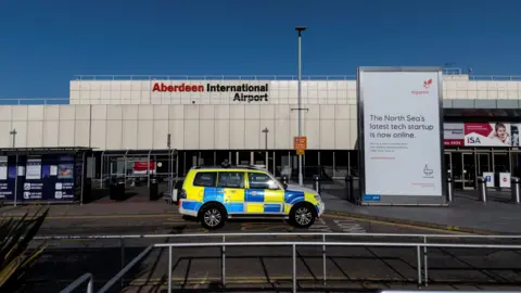 A police car in front of Aberdeen International Airport's main building on a sunny day.