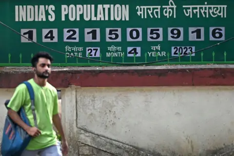 AFP via Getty Images A pedestrian walks past a population clock board displayed outside the International Institute for Population Sciences (IIPS) in Mumbai. 
