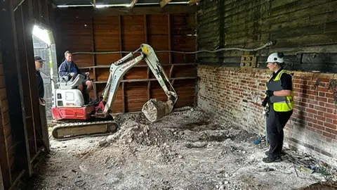 PA Media A digger in a farmyard barn