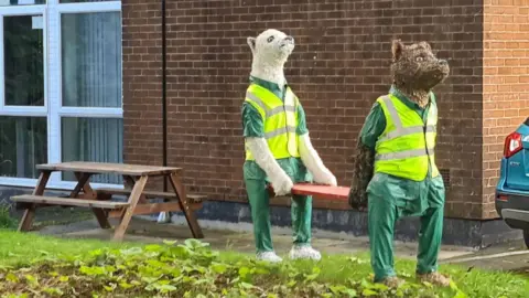 Malcolm Curley The image shows two bears, one brown and one white, dressed in paramedic uniforms and hi-vis waistcoats, holding a stretcher between them. They are positioned in the car park of the local ambulance station.