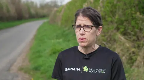 Heather Davey in a black Garmin t-shirt stood at the side of a road with green hedges and grass behind her.