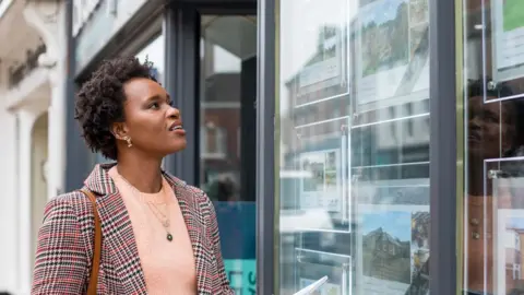 Getty Images Woman looking at pictures of properties in the window of an estate agents