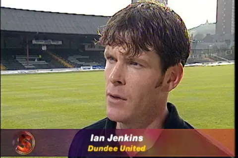 A screengrab from a TV interview from the late 1990s. It shows Iain Jenkins (the name is mis-spelled as Ian on the caption) on the pitch at Tannadice Park in Dundee