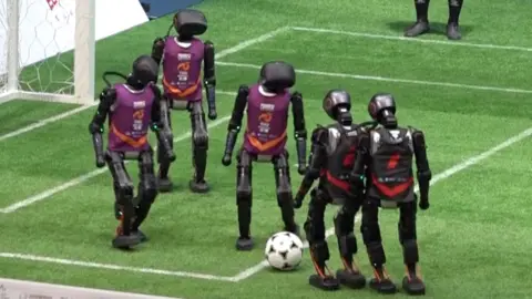 Five humanoid robots, on playing football on field