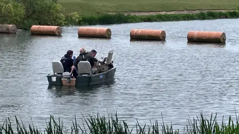 A small black boat on a river with three officers, dressed in black sat in it.