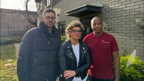 Homeowners Robert Altman, Georgina Bright and Themba Sikhosana stood outside one of the houses on Florence Close 