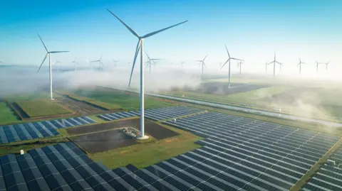 Wind turbines in fog and solar panels covering the ground.