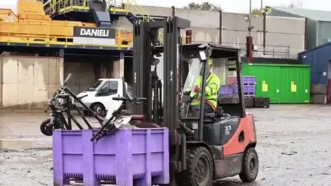Northamptonshire Police Man in high viz drives a fork lift truck which is carrying a purple crate containing e-scooters