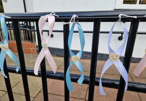 Blue, pink and lilac ribbons along a railing with white hearts in the middle with names of babies written on them