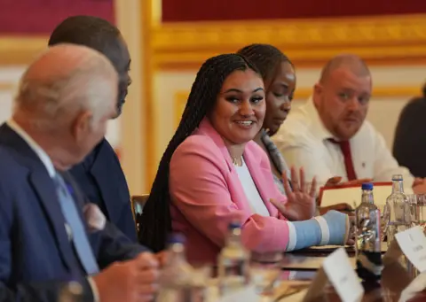 PA Media Young lady wearing a pink blazer facing the King who's head is turned away from the camera