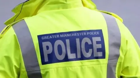 PA Media close up of the back of a high vis yellow police coat with "Greater Manchester Police" on the back in blue