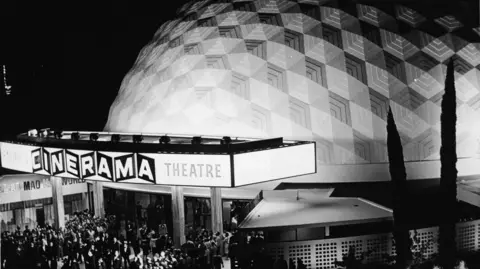 Getty Images A black and white photo from 1965 shows a crowd outside the Cinerama theatre in 1965. In the background you can see the white down.
