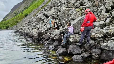 WMRT The two dogs on rocks with their owners. A boat with a rescuerer is picking them up.