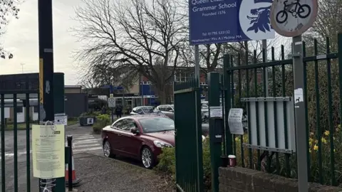 A view of the school gates at a school, with a car parked behind it.