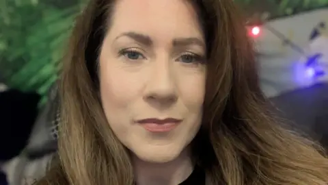 Handout A woman with long brown hair looking at the camera. Her lips are closed and she does not smile