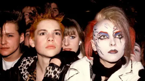 Getty Images Two young women from the early 1980s photographed facing the camera. One has blonde and red hair with elaborate make-up of a white face, red eyebrows, blue eye shadow and blue-grey lips  