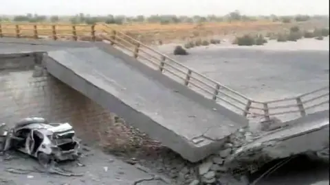 A damaged portion of the bridge in the aftermath of the overnight strike in Bandar Khamir, Hormozgan province. The image shows a portion of the bridge collapsed with rubble surrounding it, it is positioned diagonally with a damaged car