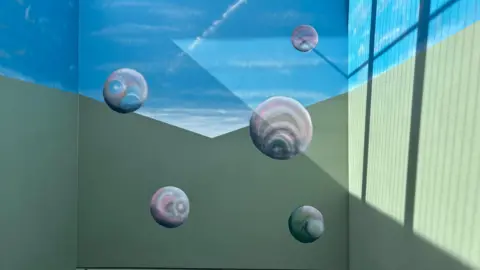 An image of three walls of the mural featuring a green base and a daylight skyline with grey balls of varying sizes.
