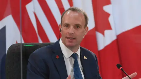 Reuters Dominic Raab delivers an address seated before a range of flags