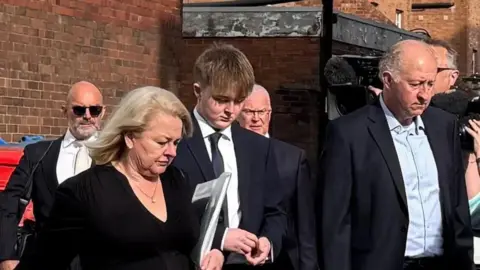 A man wearing a suit walks into court with a group of smartly dressed men and women.