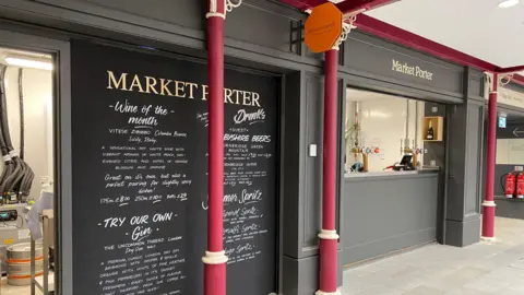 A view of a bar inside Derby Market Hall. There are red posts in front of it with the name "Market Porter" seen above