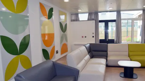 NHS Somerset Communal space at the new ward, with floral panels on the wall, soft leather sofas and a small table in the middle