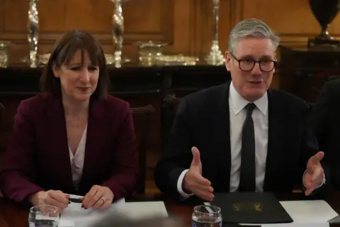 Rachel Reeves and Sir Keir Starmer both sitting at a table in Downing Street wearing suits. Sir Keir is talking and Reeves is listening