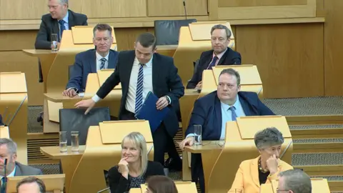 Douglas Ross standing up from his seat in the Holyrood chamber