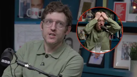 Elis James in a radio studio in front of a BBC microphone. He has brown hair and round rimmed glasses. An inset photos shows him holding his head in his hands. 