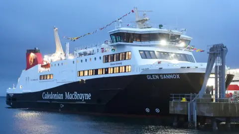 PA Media Glen Sannox ferry moored at a dock as darkness falls.