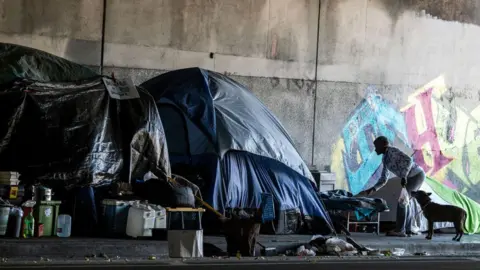 Getty Images Tents, trash cans, graffiti, person leaning over next to a dog