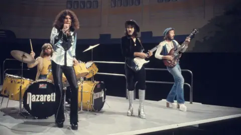 Getty Images Nazareth are playing on stage in 70s attire, including leather trousers, platform boots and hats.