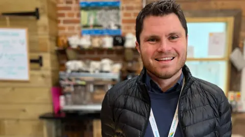 Jon Wright/BBC Cllr George King stands in front of the farm café counter