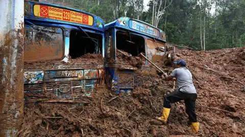 AFP via Getty Images A worker removes mud accumulated around buses near a landslide-affected area in the aftermath of Cyclone Ditwah, in Maspanna on December 13, 2025.