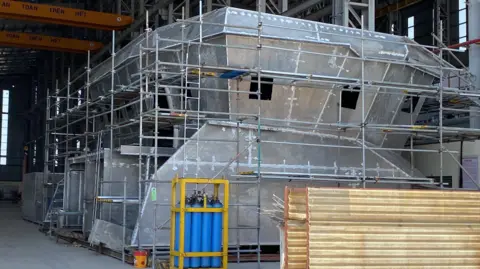 Isles of Scilly Steamship Group Unpainted steel wheelhouse of new vessel surrounded by scaffolding. It is sitting in a boatyard shed in Vietnam yet to be lowered on  to the vessel  