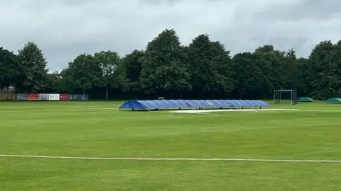 A cricket pitch with a blue cover over the wicket.