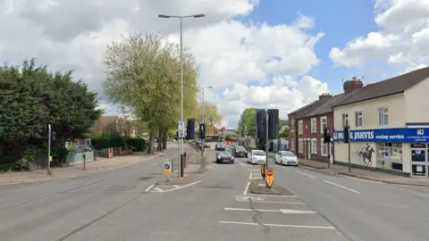 Google A city dual carriageway showing cars stopped at the traffic lights and a betting shop.  