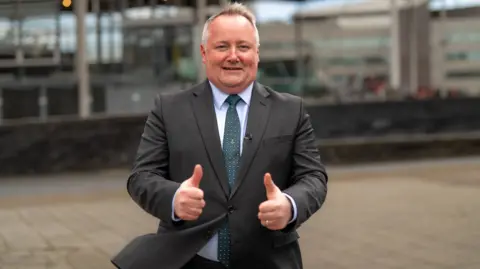 Darren Millar wearing a suit with his thumbs up