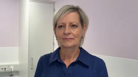 A woman with greying shoulder-length hair looks just past the camera.