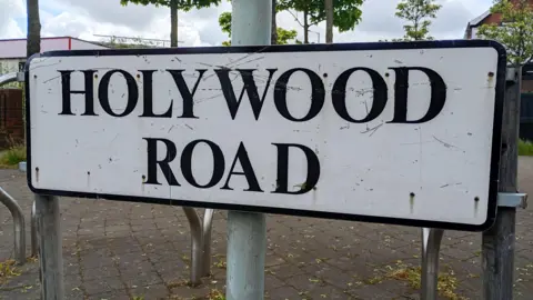 White road sign with black text which says 'Holywood Road'
