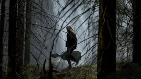 Visit Finland Girl calmly walking through a Finnish forest in the dark with her instrument