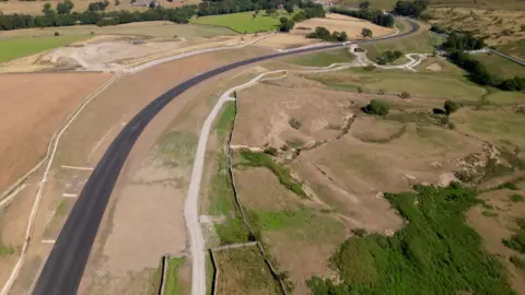 An aerial view of the new Kex Gill bypass, a tarmacked road running through a predominantly rural area with fields and moorland on either side.