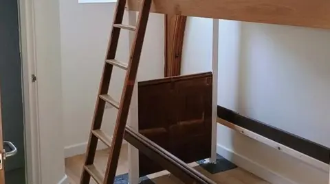 LDRS A small room with a set of bunk beds made from wood with a door to the left leading to a private shower