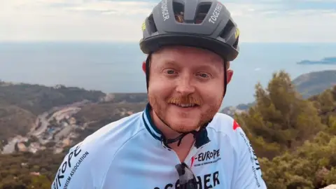 Travis Frain Travis Frain wearing a cycling helmet with French mountain views in the background