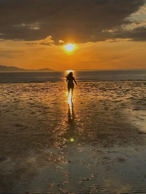 Fiona Taylor A person runs into the sea as the sun sets