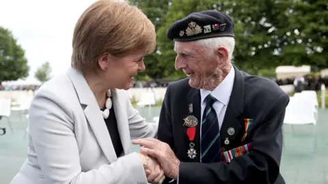 Jane Barlow First Minister Nicola Sturgeon sits with D-Day veteran John Greig, 95, from Dumfries, at the Commonwealth War Graves Commission Cemetery in Bayeux