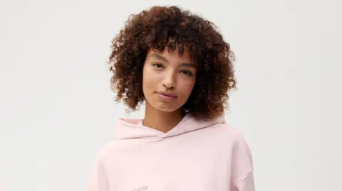 Colorifix/Pangaia A model with short curly hair wearing a pale pink hoodie.