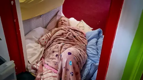 Family photo Theresa Jones wrapped in a blanket and lying on the floor in a doorway beside a bed