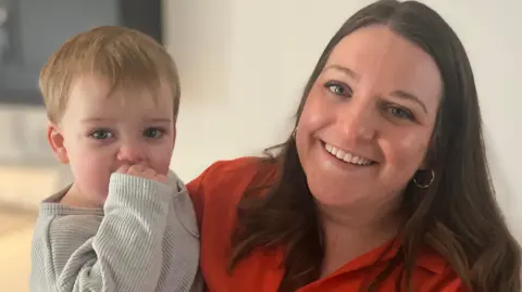 Kim McKinnon holding her child 18-month-old Rowan, both looking at the camera.